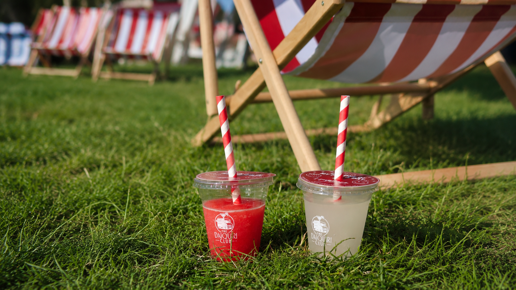 Two branded Daiquiri Club cups on the grass in front of a red-and-white striped deckchair