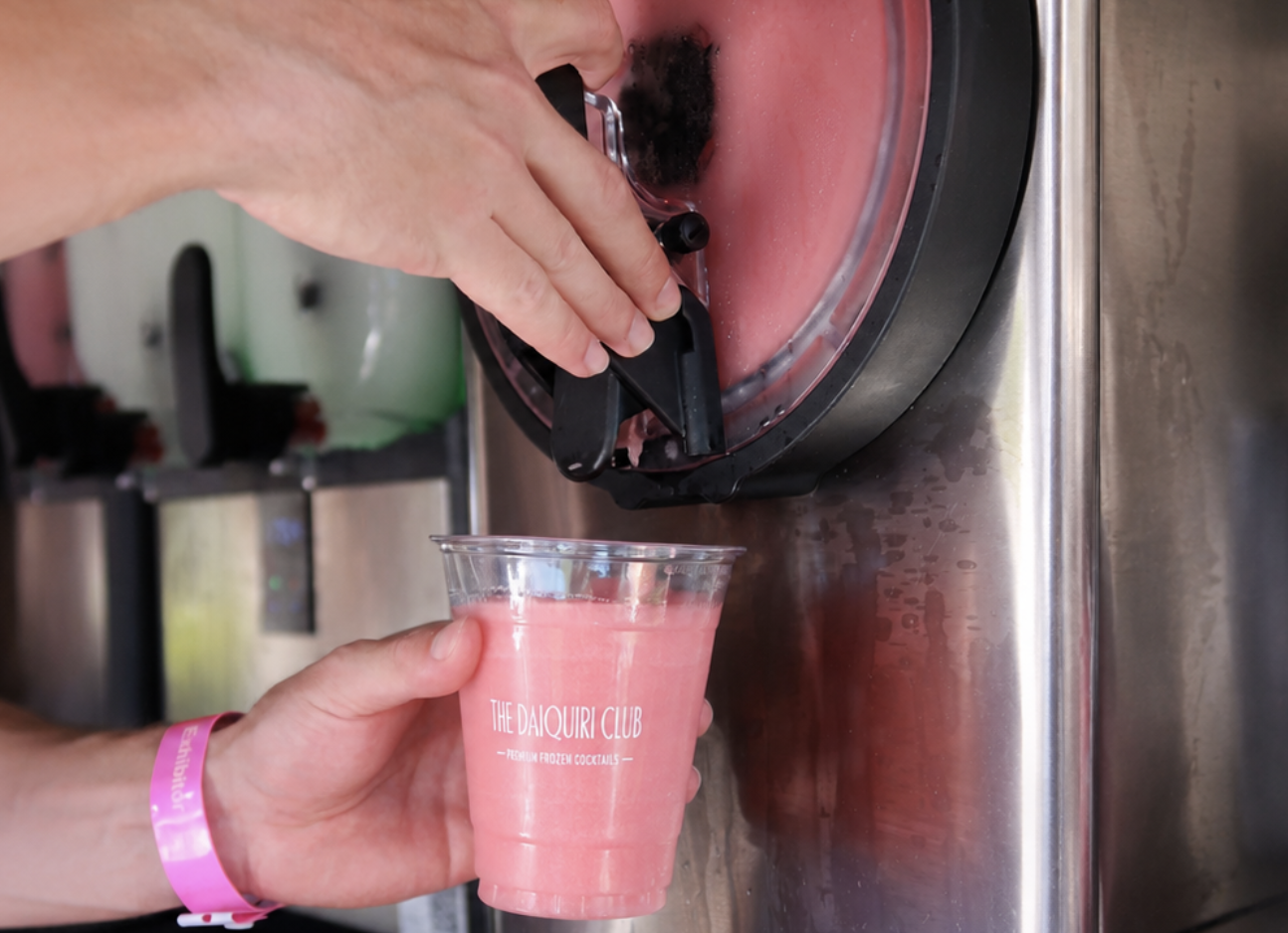 Frozen strawberry daiquiri being poured from the slush machine into a branded Daiquiri Club cup